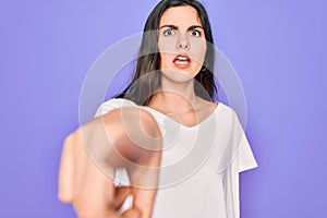 Young beautiful brunette woman wearing casual white t-shirt over purple background pointing displeased and frustrated to the