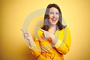 Young beautiful brunette woman wearing elegant dress over yellow isolated background smiling and looking at the camera pointing