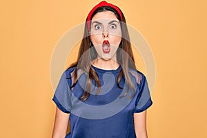 Young beautiful brunette woman wearing red lips over yellow background afraid and shocked with surprise expression, fear and