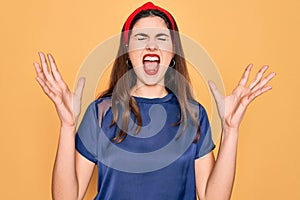 Young beautiful brunette woman wearing red lips over yellow background celebrating mad and crazy for success with arms raised and