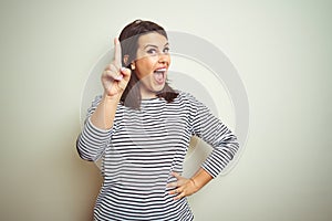 Young beautiful brunette woman wearing striped sweater over white isolated background pointing finger up with successful idea