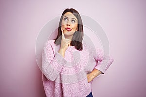 Young beautiful brunette woman wearing a sweater over pink isolated background with hand on chin thinking about question, pensive