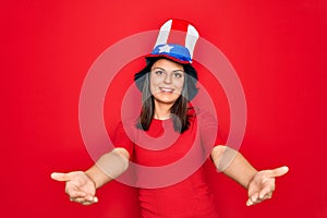 Young beautiful brunette woman wearing united states hat celebrating independence day smiling cheerful offering hands giving