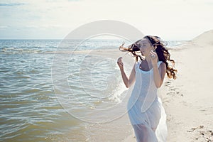 Young beautiful brunette woman in white dress on the seashore