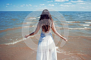 Young beautiful brunette woman in white dress on the seashore.