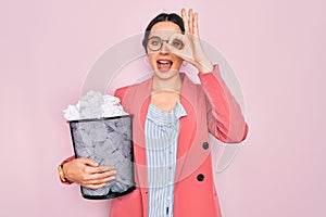 Young beautiful business woman with blue eyes holding heap bin of crumpled papers with happy face smiling doing ok sign with hand