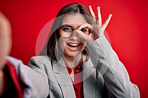 Young beautiful business woman with blue eyes wearing glasses making selfie by camera with happy face smiling doing ok sign with