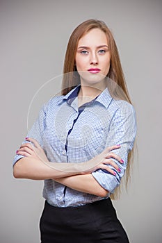 Young beautiful business woman in a blue shirt stands with her arms crossed and thinks over a gray background