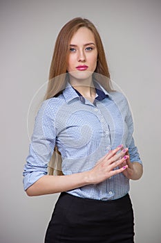 Young beautiful business woman in a blue shirt stands with her arms crossed and thinks over a gray background