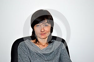 Young beautiful business woman in gray dress sitting on the black leather armchair and confidently looking into the camera