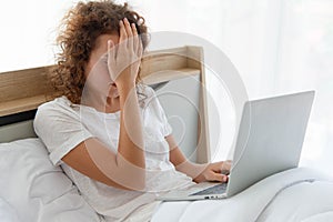 Young beautiful business woman has headache working with laptop while lying in bed in the morning after waking up