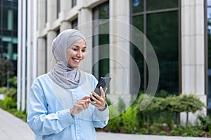 Young beautiful business woman in hijab walks in the city outside the office building, Muslim woman uses an application