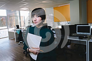 Young beautiful business woman posing with papers on the background of office space. Secretary with documents.