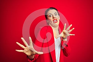 Young beautiful business woman standing over red isolated background afraid and terrified with fear expression stop gesture with