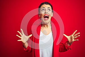 Young beautiful business woman standing over red isolated background crazy and mad shouting and yelling with aggressive expression