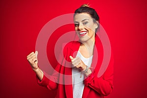 Young beautiful business woman standing over red isolated background Pointing to the back behind with hand and thumbs up, smiling