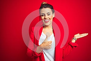 Young beautiful business woman standing over red isolated background Showing palm hand and doing ok gesture with thumbs up,