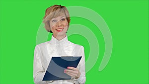 Young beautiful business woman in a suit, smiling, happy, working with a tablet, writing a message on a Green Screen