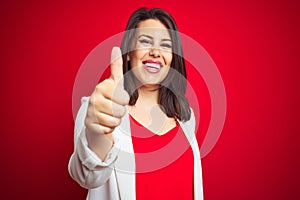 Young beautiful business woman wearing elegant jacket over red isolated background doing happy thumbs up gesture with hand