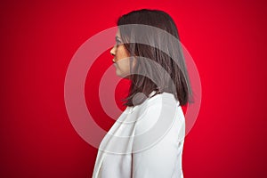 Young beautiful business woman wearing elegant jacket over red isolated background looking to side, relax profile pose with