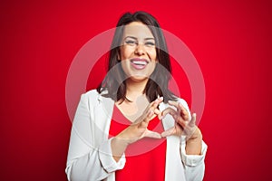 Young beautiful business woman wearing elegant jacket over red isolated background smiling in love showing heart symbol and shape