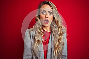 Young beautiful business woman wearing elegant jacket standing over red isolated background afraid and shocked with surprise
