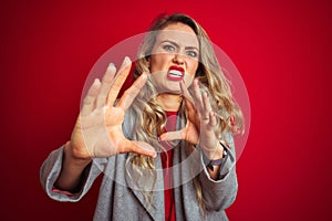 Young beautiful business woman wearing elegant jacket standing over red isolated background afraid and terrified with fear