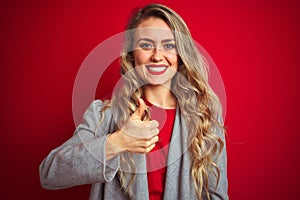 Young beautiful business woman wearing elegant jacket standing over red isolated background doing happy thumbs up gesture with