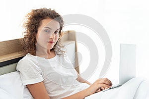 Young beautiful business woman working with laptop while lying in bed in the morning after waking up
