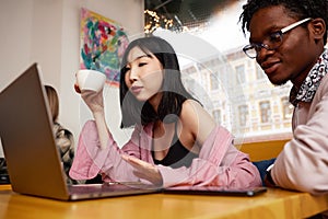 Young beautiful business woman works remotely on a laptop in a cafe, drinks coffee.