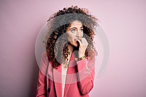 Young beautiful businesswoman with curly hair and piercing wearing elegant jacket looking stressed and nervous with hands on mouth