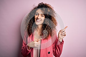 Young beautiful businesswoman with curly hair and piercing wearing elegant jacket smiling and looking at the camera pointing with