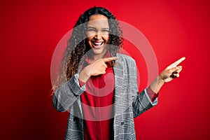 Young beautiful businesswoman with curly hair wearing elegant jacket over red background smiling and looking at the camera