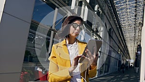 Young beautiful businesswoman in headphones using tablet computer standing on the urban street at the business centre