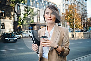 Young beautiful businesswoman with laptop and coffee to go on street