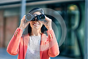 Young beautiful businesswoman smiling happy looking for new opportunities using binoculars at the city