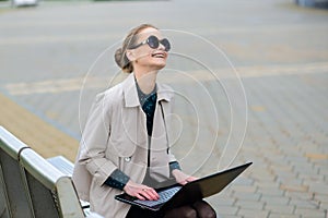 Young beautiful businesswoman with sunglasses, phone, laptop, cup of coffee in the city streets