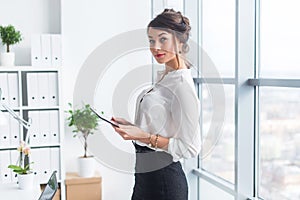 Young beautiful businesswoman using tablet with internet in office, reading and sending messages, smiling, looking at