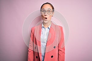 Young beautiful businesswoman wearing jacket and glasses over isolated pink background afraid and shocked with surprise