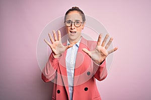 Young beautiful businesswoman wearing jacket and glasses over isolated pink background afraid and terrified with fear expression