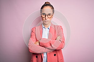 Young beautiful businesswoman wearing jacket and glasses over isolated pink background skeptic and nervous, disapproving