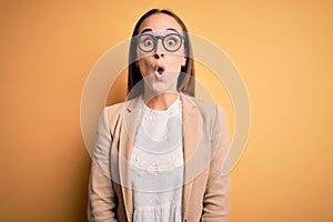 Young beautiful businesswoman wearing jacket and glasses over isolated yellow background afraid and shocked with surprise