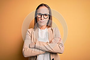 Young beautiful businesswoman wearing jacket and glasses over isolated yellow background skeptic and nervous, disapproving