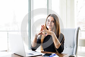 Young beautiful businesswoman working on laptop and keeping hand on chin while sitting at her working place