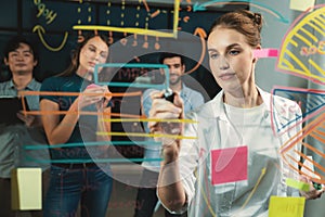 Young beautiful businesswoman writing business plan on glass wall. Tracery.