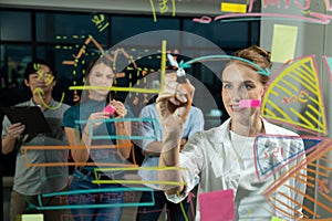 Young beautiful businesswoman writing business plan on glass wall. Tracery.