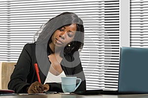 Young beautiful and busy black African American businesswoman writing notes on desk working with laptop computer at company office