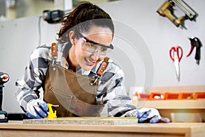 Young beautiful carpenter woman with apron holding yellow tape measure for measuring wood plank, female craft worker making wooden