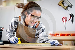 Young beautiful carpenter woman with apron holding yellow tape measure for measuring wood plank, female craft worker making wooden