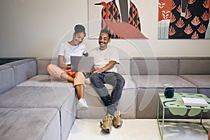 Young beautiful casual African American couple happily watching movie on laptop at home